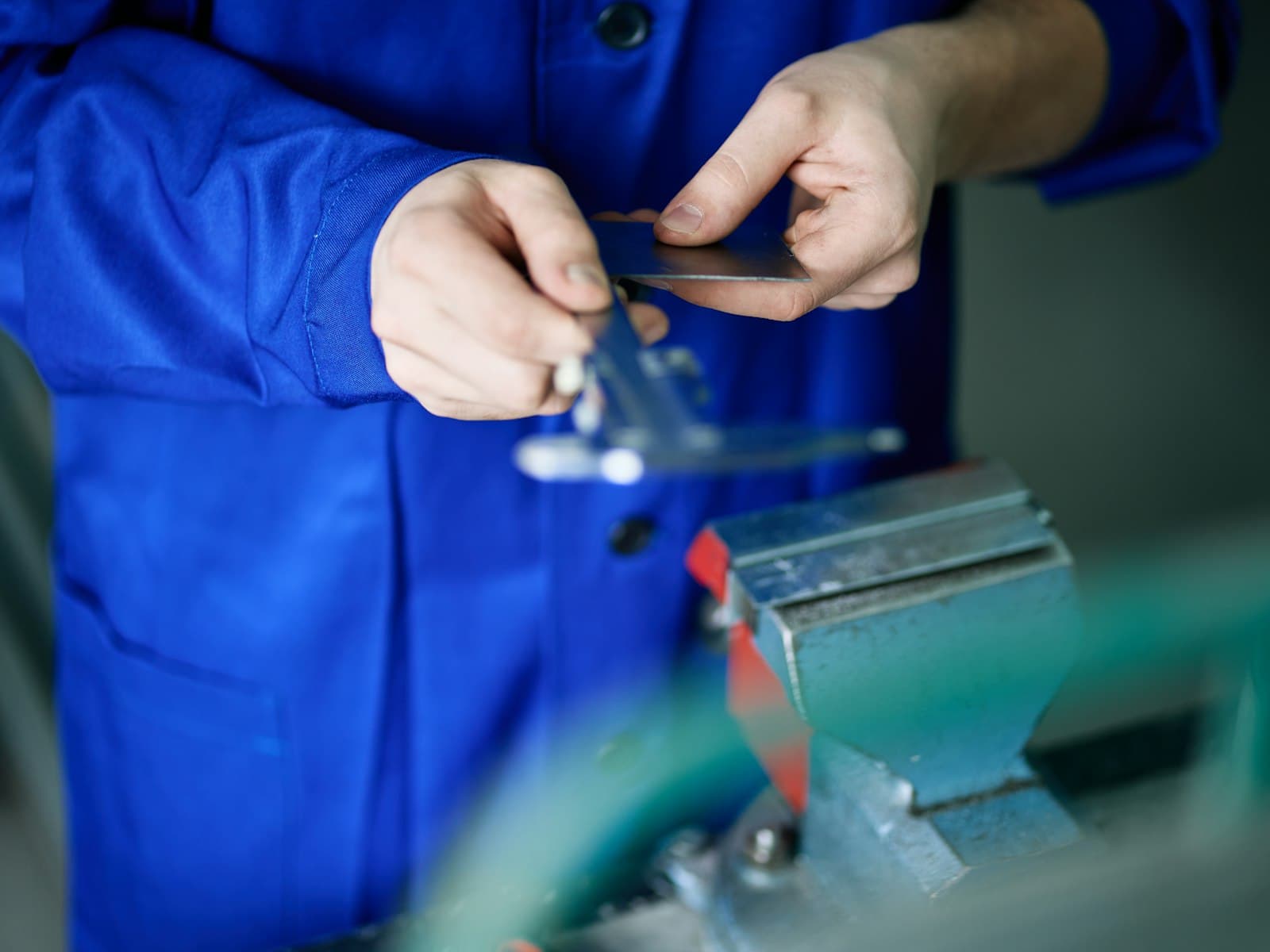 Worker in blue overalls measuring a small metal part with calipers