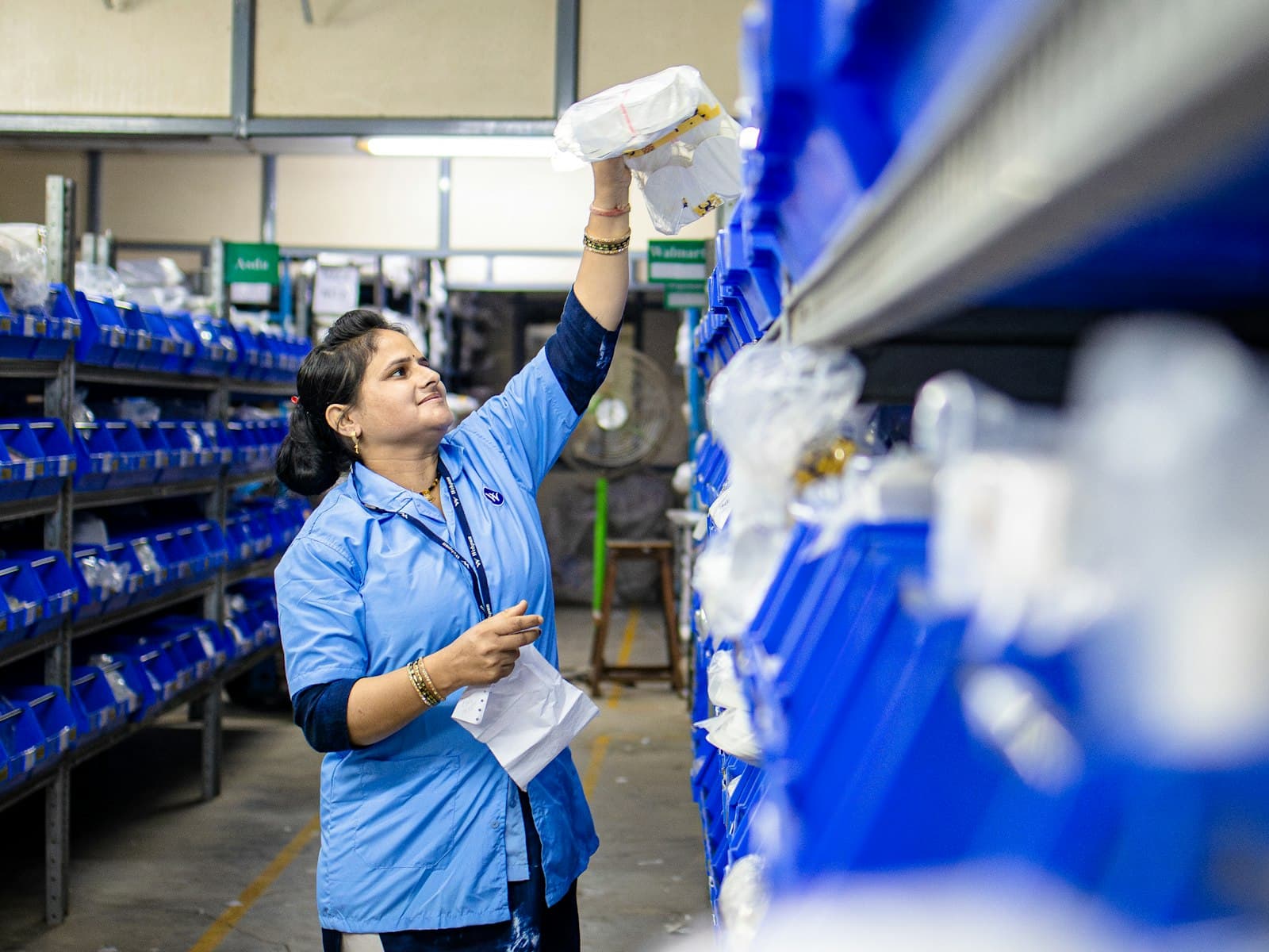 Warehouse worker reaching for an item on high shelving while holding a pick list